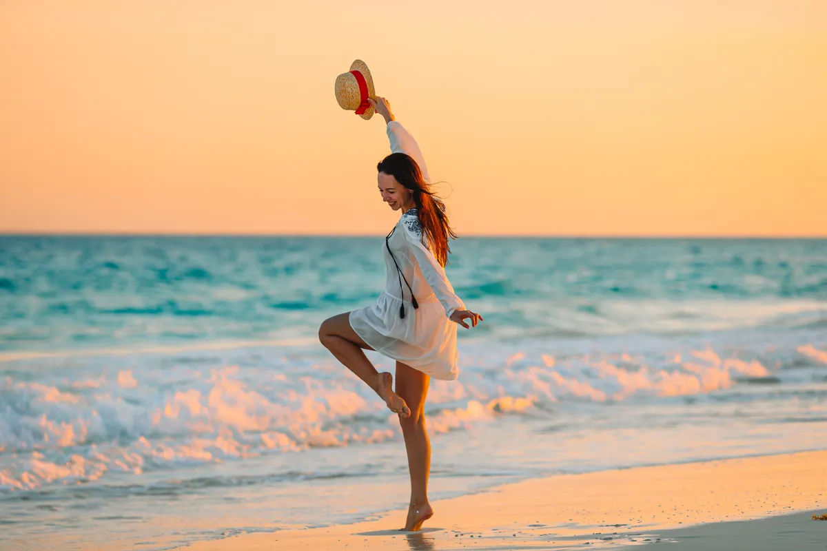 Mulher feliz na praia ao pôr do sol, representando bem-estar e saúde